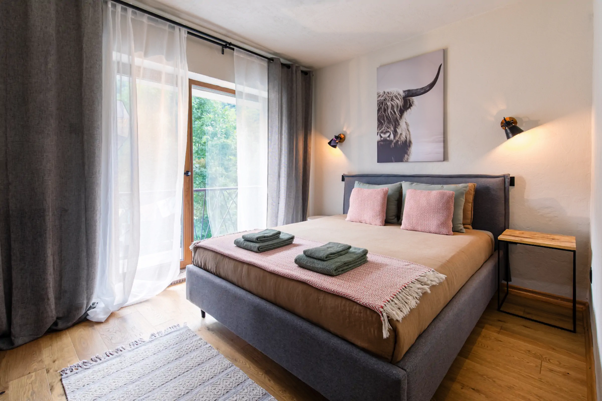 Cozy master bedroom with modern black bed frame, pink accents, Highland cow artwork, and balcony access at Fireside Lodge