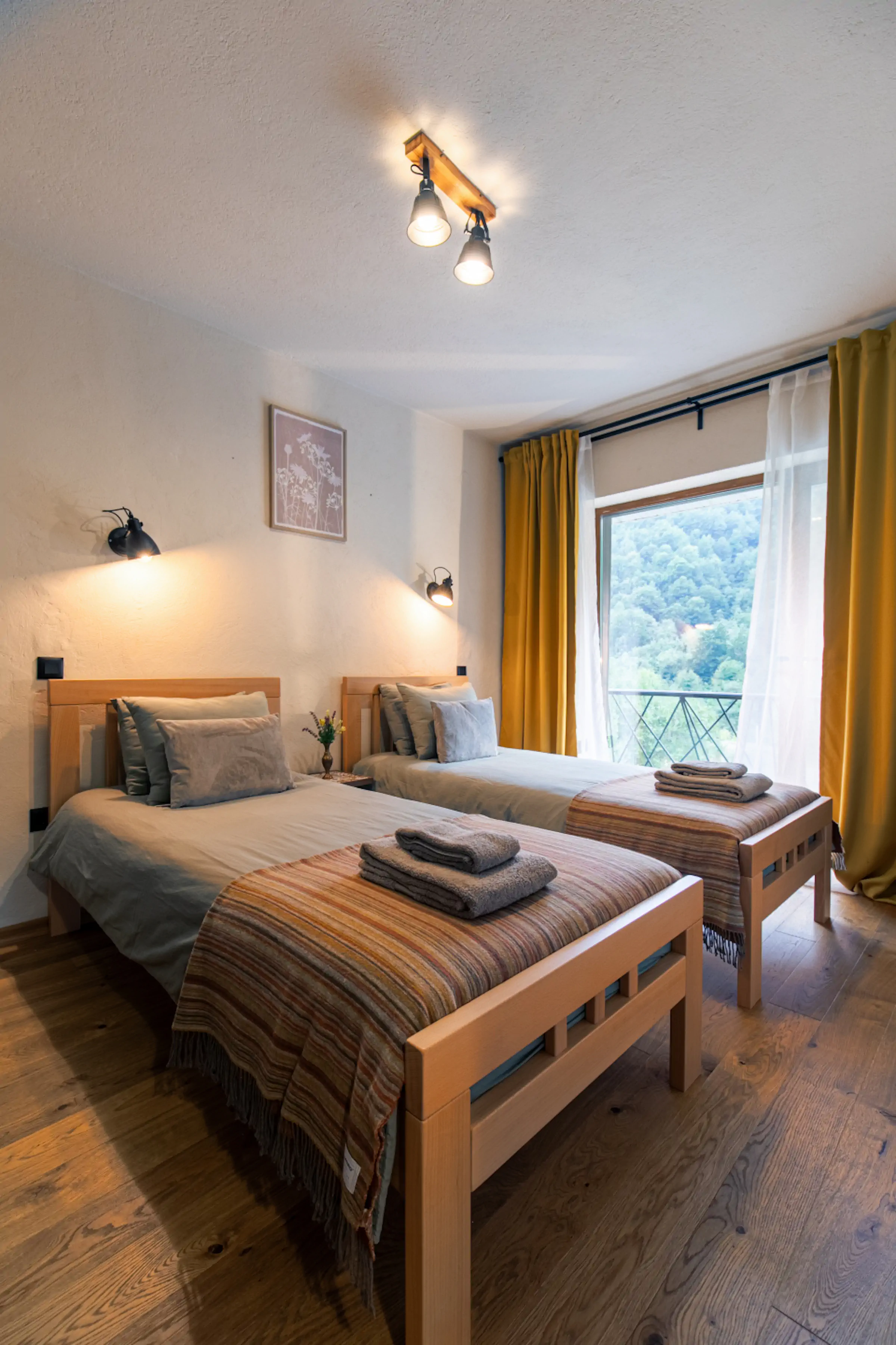 Twin bedroom with wooden beds, mustard yellow curtains, and mountain valley views from windows at Fireside Lodge Montenegro