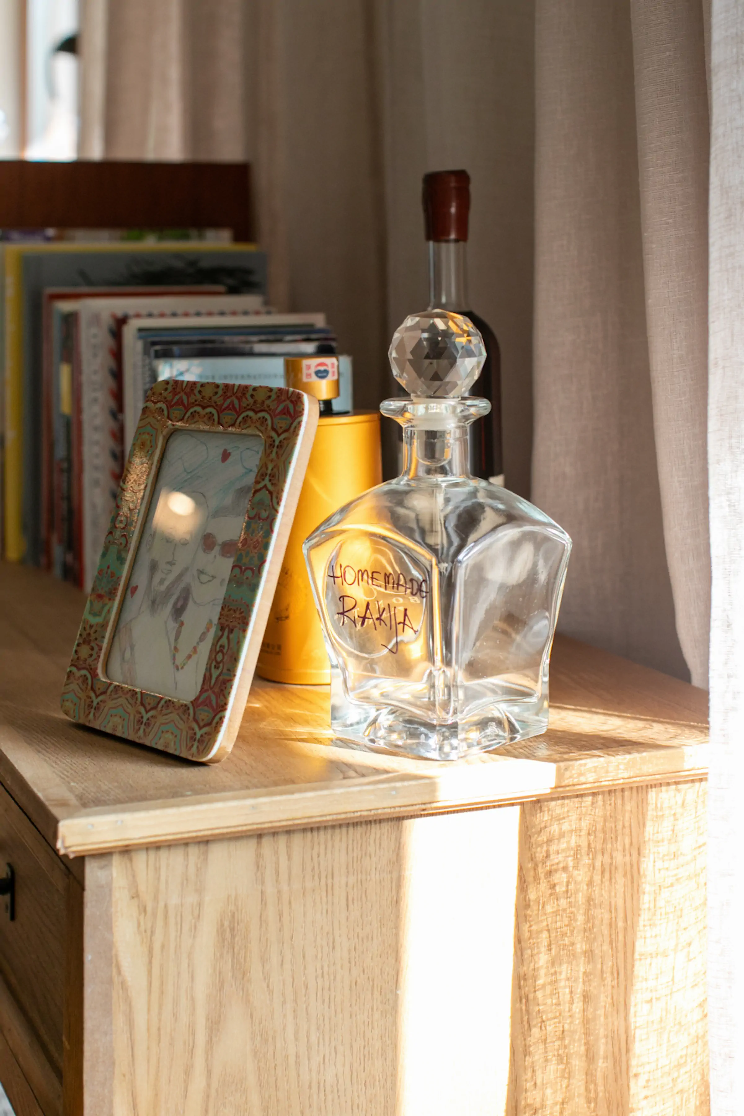 Homemade rakija liquor decanter with vintage frames and books on wooden shelf displaying local Montenegro hospitality at Fireside Lodge