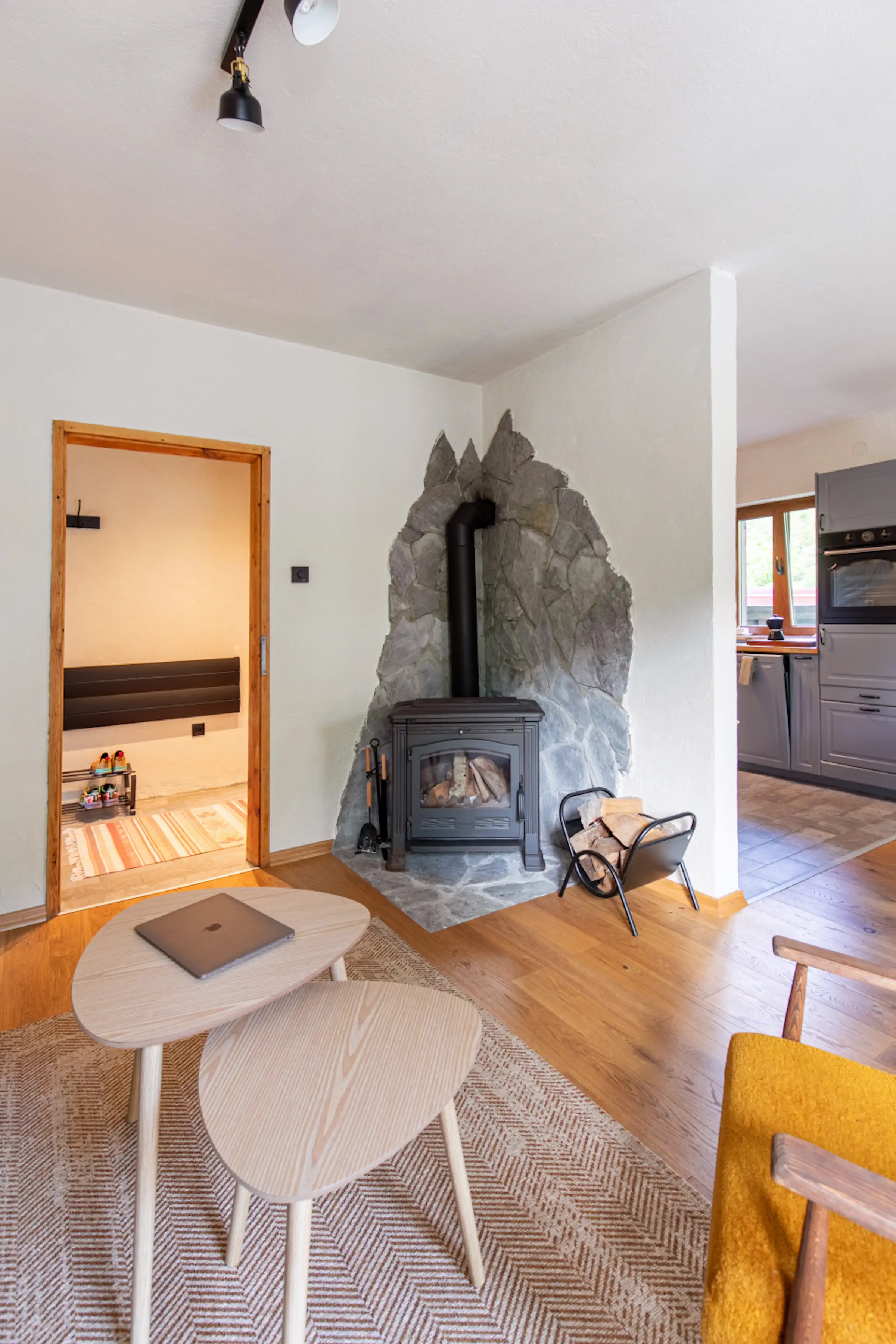 Living room stone fireplace detail with mustard mid-century armchair, open floor plan to dining and kitchen at Fireside Lodge