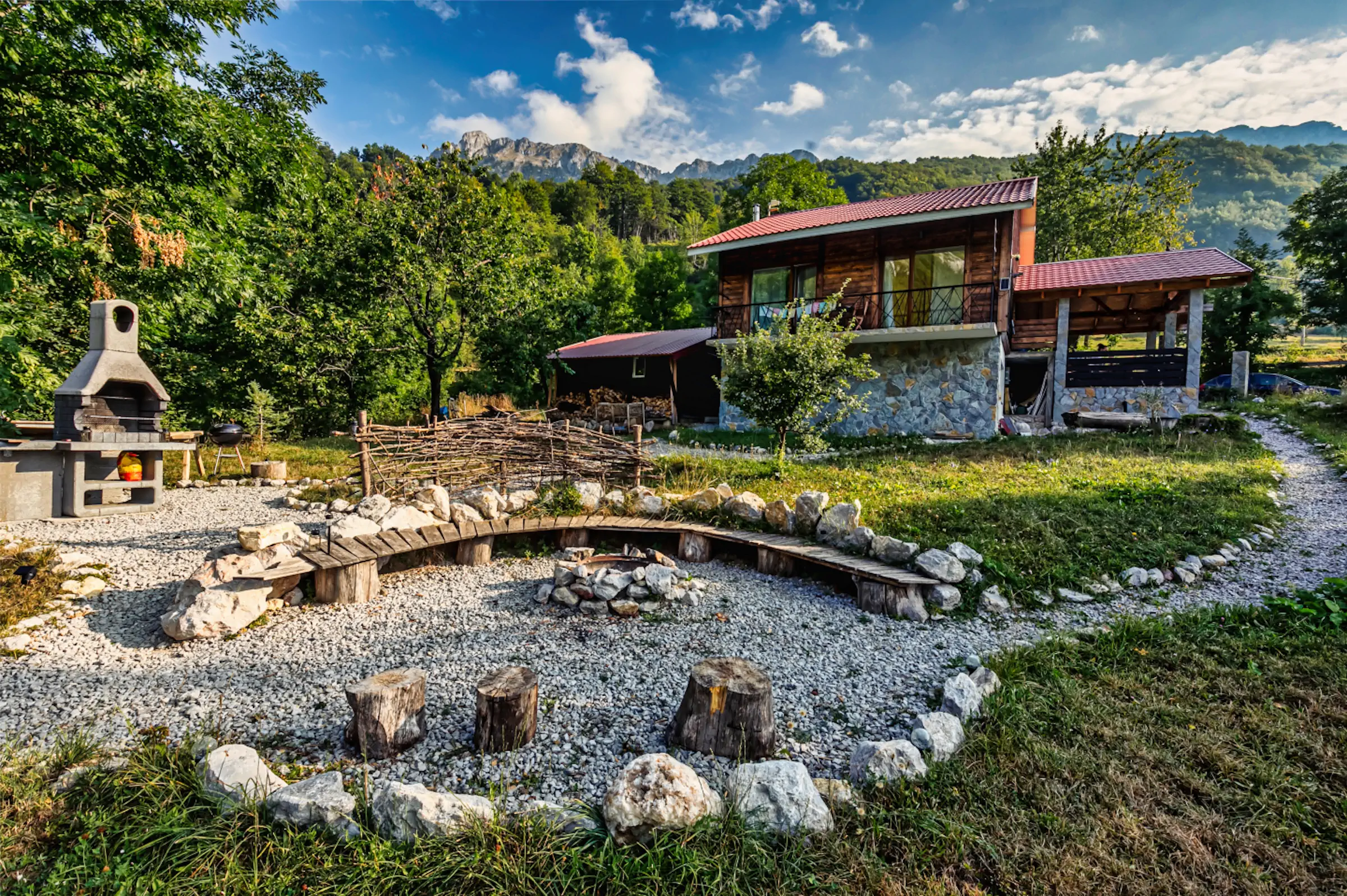 Fireside Lodge exterior with stone BBQ fireplace, circular fire pit seating area, and Montenegro mountain backdrop in Lipovo Valley