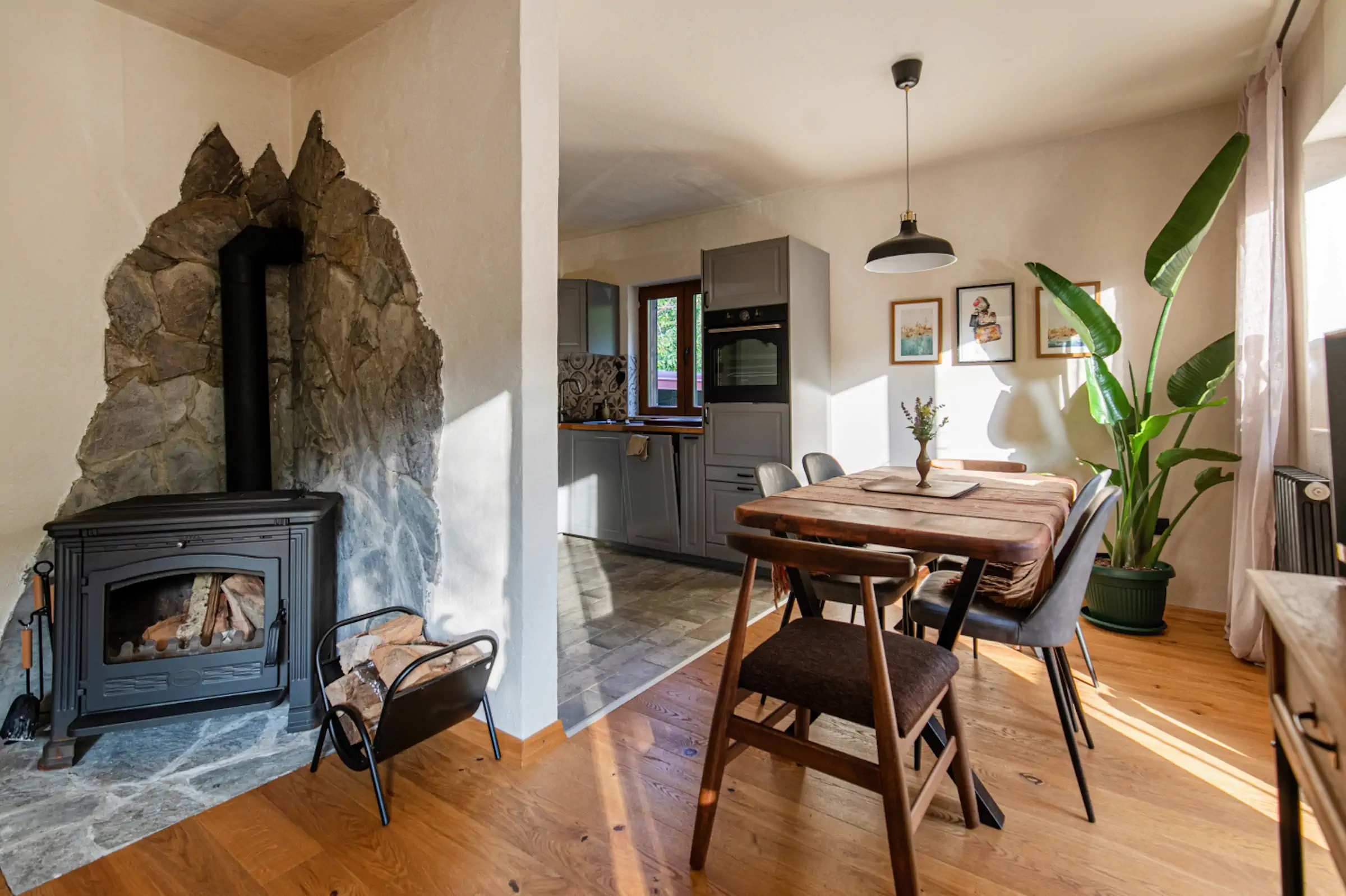 Modern living room with dramatic stone fireplace feature wall, wood stove, open kitchen, and mid-century dining furniture at Fireside Lodge